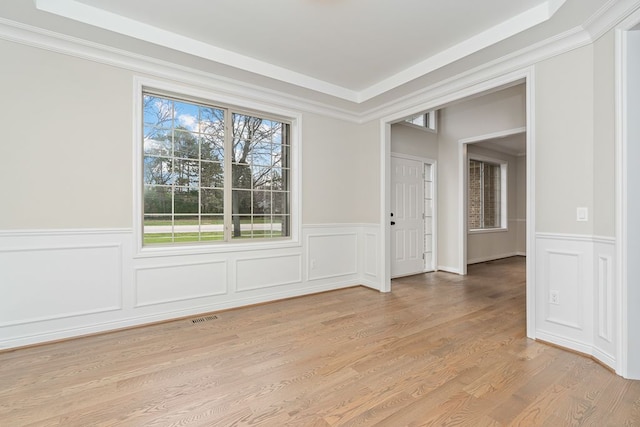 unfurnished room with light wood-type flooring, a tray ceiling, and ornamental molding