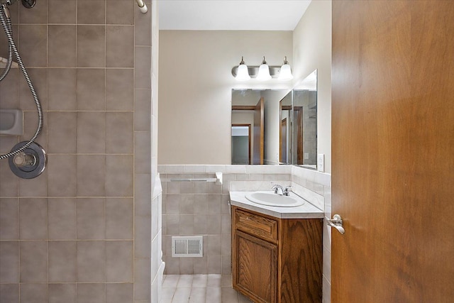 bathroom with tile patterned floors, vanity, tiled shower, and tile walls