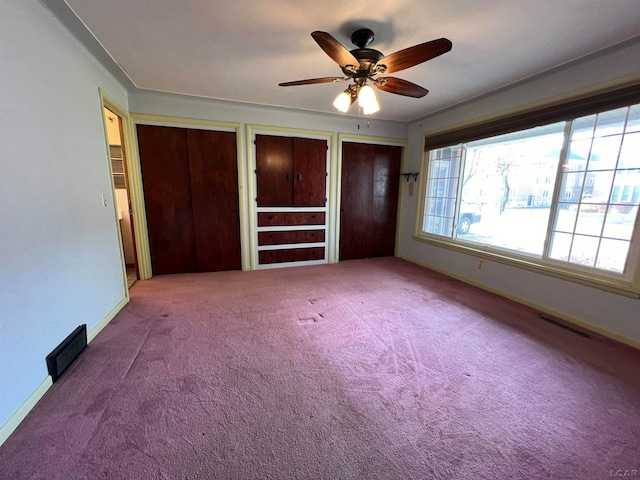 unfurnished bedroom featuring ceiling fan, carpet, and two closets