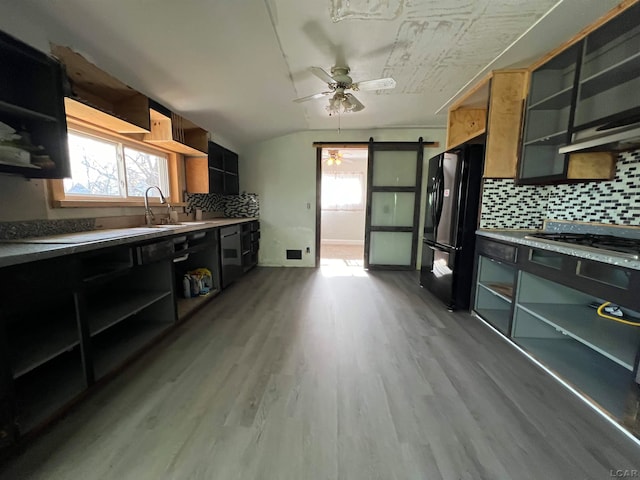 kitchen with decorative backsplash, black fridge, ceiling fan, a barn door, and light hardwood / wood-style floors