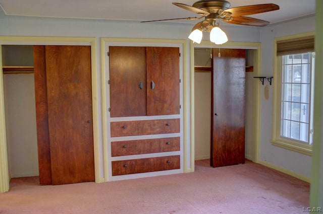 unfurnished bedroom featuring light colored carpet, ceiling fan, and multiple closets