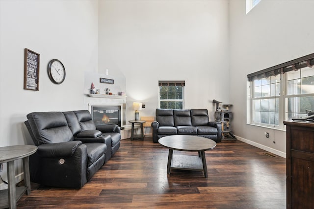 living room featuring a wealth of natural light, a towering ceiling, and dark wood-type flooring