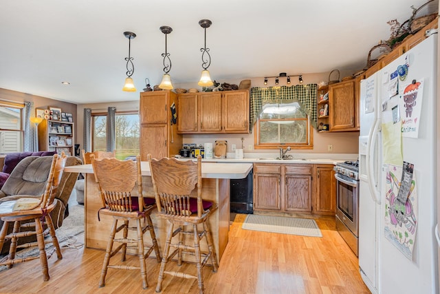 kitchen with decorative light fixtures, sink, a kitchen breakfast bar, white fridge with ice dispenser, and gas range