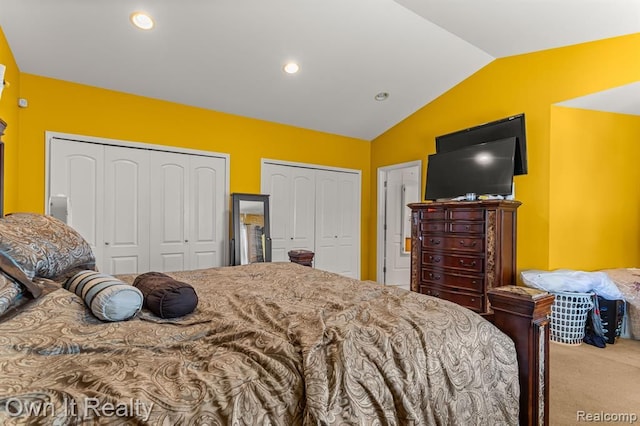 bedroom with light colored carpet, lofted ceiling, and two closets