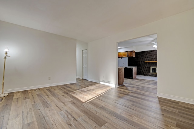 empty room featuring a fireplace, light wood-type flooring, ceiling fan, and brick wall