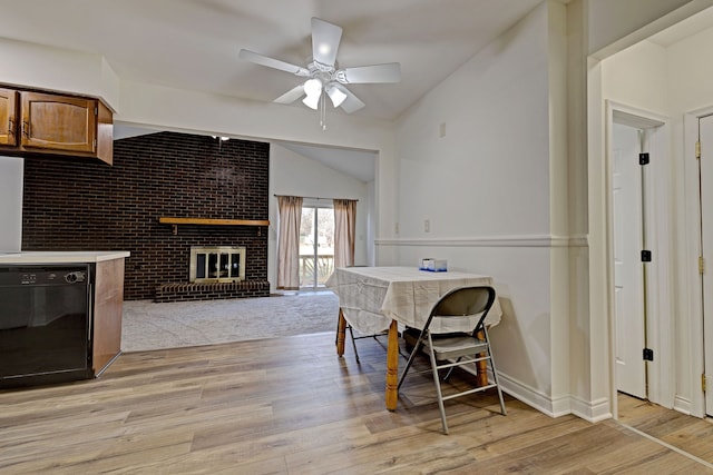 dining room featuring ceiling fan, light wood-type flooring, a fireplace, and vaulted ceiling