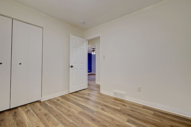 unfurnished bedroom with crown molding, a closet, and light wood-type flooring