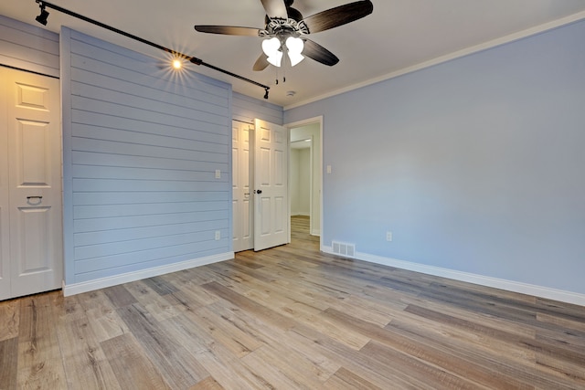 unfurnished bedroom featuring light hardwood / wood-style flooring, ceiling fan, wooden walls, and crown molding