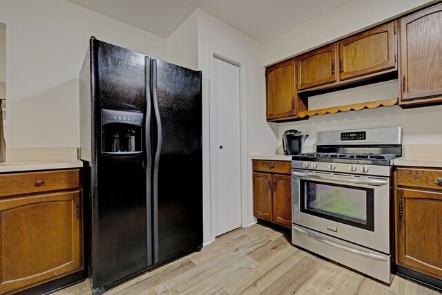 kitchen featuring stainless steel gas stove, light hardwood / wood-style floors, and black fridge with ice dispenser