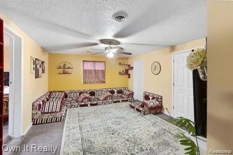 living room featuring ceiling fan, carpet floors, and a textured ceiling