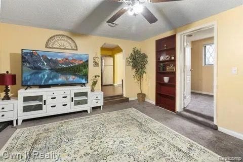 living room featuring ceiling fan, dark carpet, and a textured ceiling