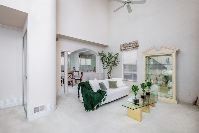 carpeted living room featuring a towering ceiling, a wealth of natural light, ornamental molding, and ceiling fan