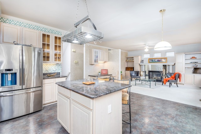 kitchen featuring stainless steel fridge, dark stone counters, decorative backsplash, a kitchen island, and ornamental molding