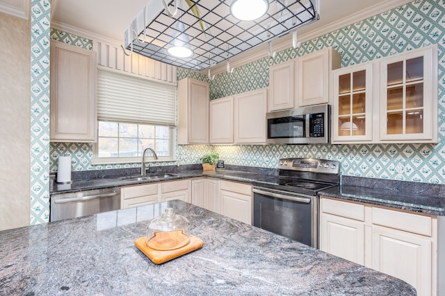 kitchen with appliances with stainless steel finishes, ornamental molding, dark stone counters, and sink