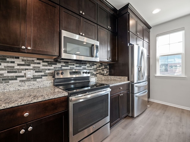 kitchen with dark brown cabinetry, stainless steel appliances, light stone counters, light hardwood / wood-style floors, and decorative backsplash