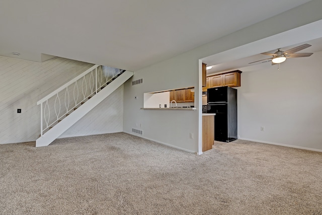 unfurnished living room with light carpet, sink, ceiling fan, and wood walls