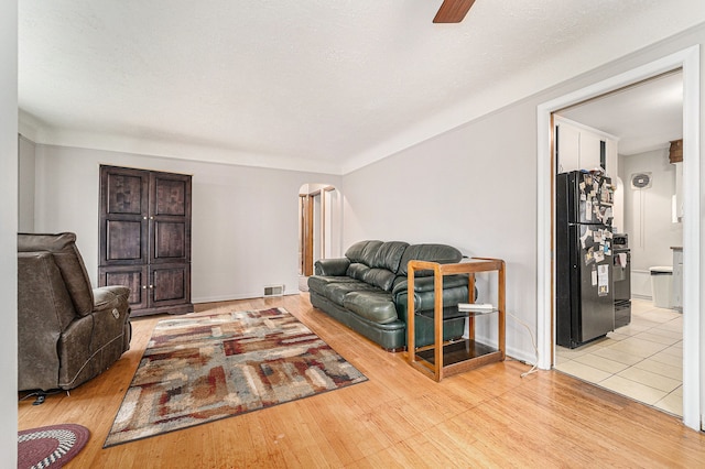 living room featuring ceiling fan, light hardwood / wood-style floors, and a textured ceiling