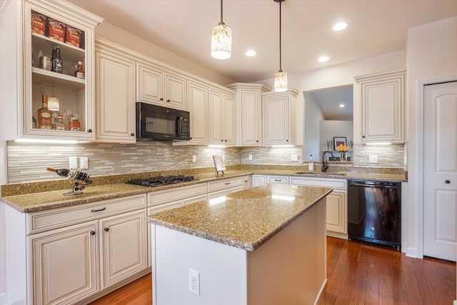 kitchen featuring hardwood / wood-style flooring, hanging light fixtures, a kitchen island, black appliances, and sink