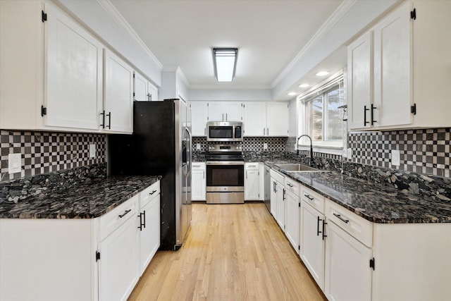 kitchen with dark stone counters, stainless steel appliances, crown molding, sink, and white cabinetry