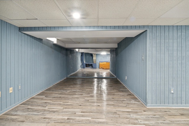 hallway with a paneled ceiling, wood walls, and hardwood / wood-style floors