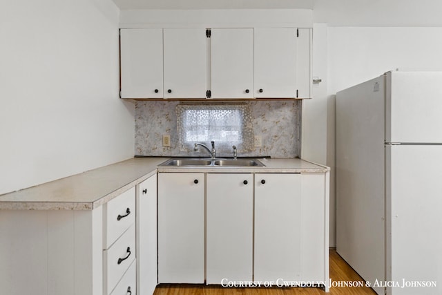 kitchen featuring white cabinetry, sink, light hardwood / wood-style flooring, backsplash, and refrigerator