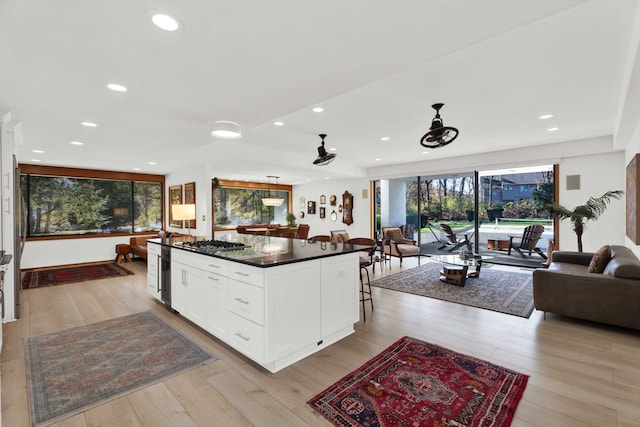 kitchen featuring white cabinetry, a center island, light hardwood / wood-style floors, stainless steel gas stovetop, and a kitchen bar