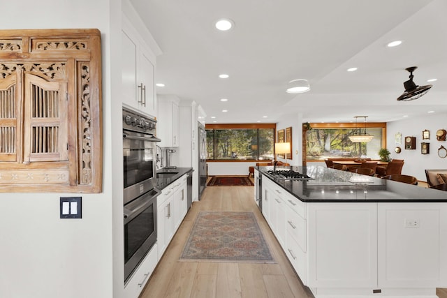 kitchen featuring white cabinetry, a center island, hanging light fixtures, light wood-type flooring, and appliances with stainless steel finishes