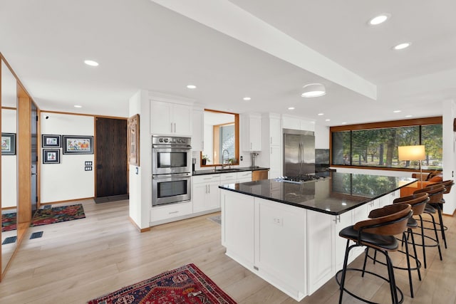 kitchen with appliances with stainless steel finishes, light hardwood / wood-style flooring, white cabinetry, and a kitchen island