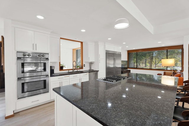 kitchen with appliances with stainless steel finishes, dark stone counters, sink, light hardwood / wood-style floors, and white cabinetry