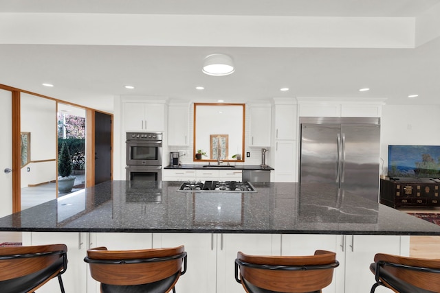 kitchen featuring a kitchen breakfast bar, dark stone countertops, white cabinetry, and appliances with stainless steel finishes