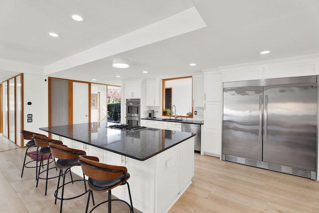 kitchen with white cabinets, sink, light wood-type flooring, appliances with stainless steel finishes, and a kitchen island