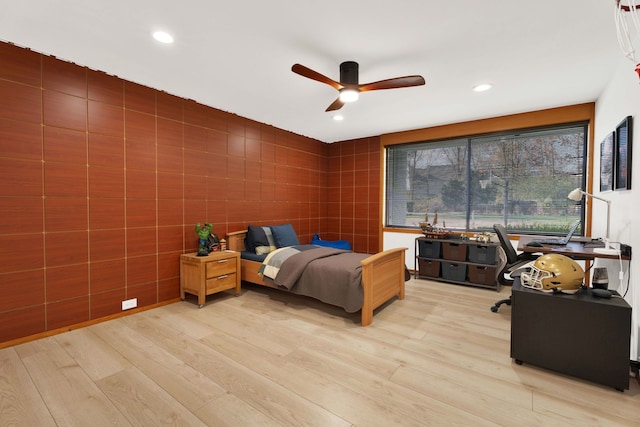 bedroom with ceiling fan, light hardwood / wood-style floors, and tile walls