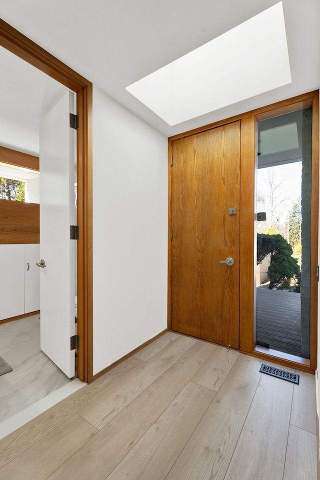 foyer entrance featuring a healthy amount of sunlight, a skylight, and light hardwood / wood-style flooring