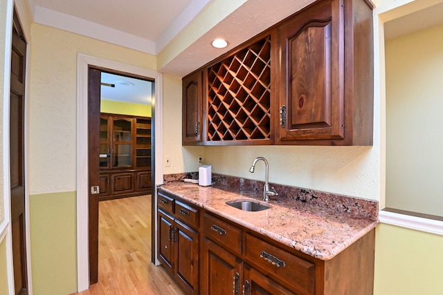 bar with sink, light stone counters, and light hardwood / wood-style floors