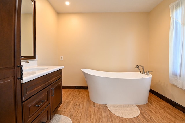 full bathroom with wood finished floors, baseboards, vanity, a soaking tub, and recessed lighting