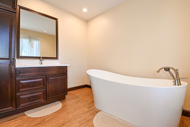 bathroom with a freestanding bath, vanity, recessed lighting, baseboards, and wood finished floors