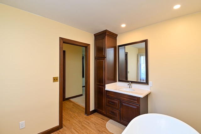 bathroom with vanity, recessed lighting, a freestanding bath, and wood finished floors