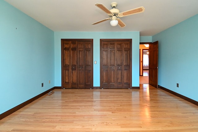 unfurnished bedroom with two closets, baseboards, ceiling fan, and light wood-style floors