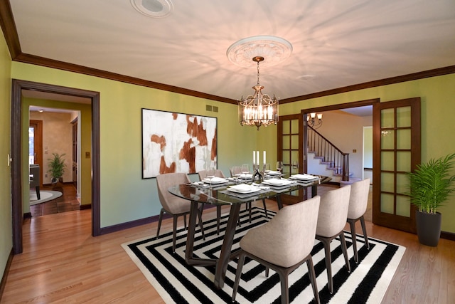 dining area featuring an inviting chandelier, crown molding, light hardwood / wood-style floors, and french doors