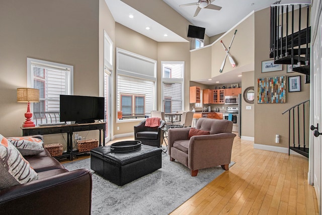 living room with ceiling fan, light hardwood / wood-style flooring, and a towering ceiling