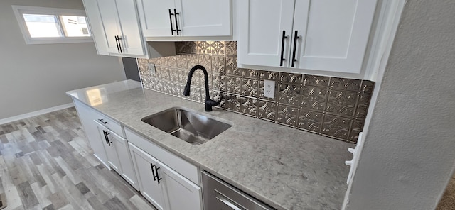 kitchen with sink, light wood-type flooring, light stone countertops, tasteful backsplash, and white cabinetry