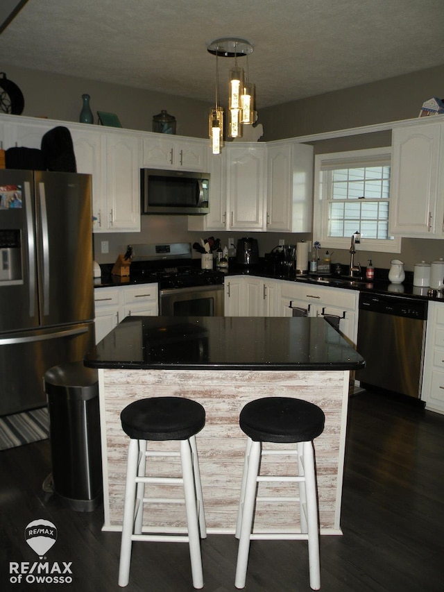 kitchen featuring pendant lighting, white cabinets, sink, dark hardwood / wood-style floors, and appliances with stainless steel finishes