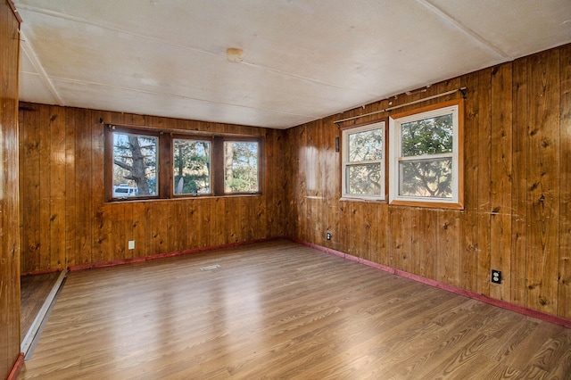 spare room with a healthy amount of sunlight, wood-type flooring, and wood walls