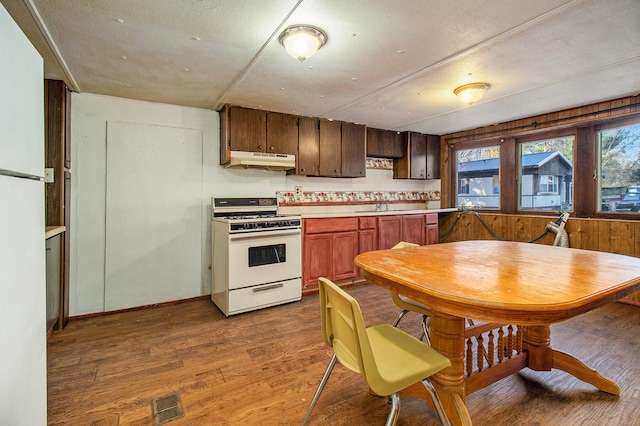 kitchen featuring wood walls, sink, a textured ceiling, white range oven, and wood-type flooring