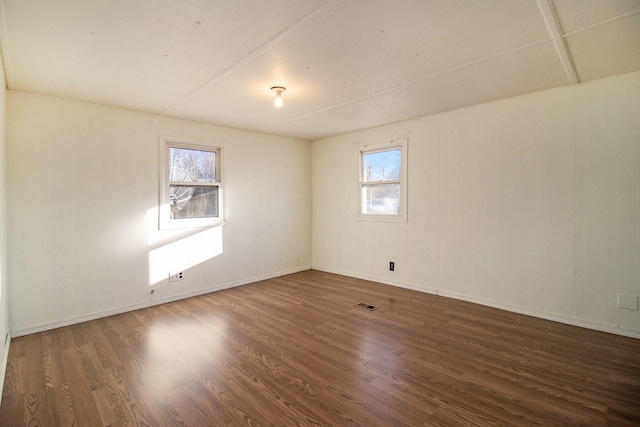 empty room with a wealth of natural light and dark hardwood / wood-style flooring