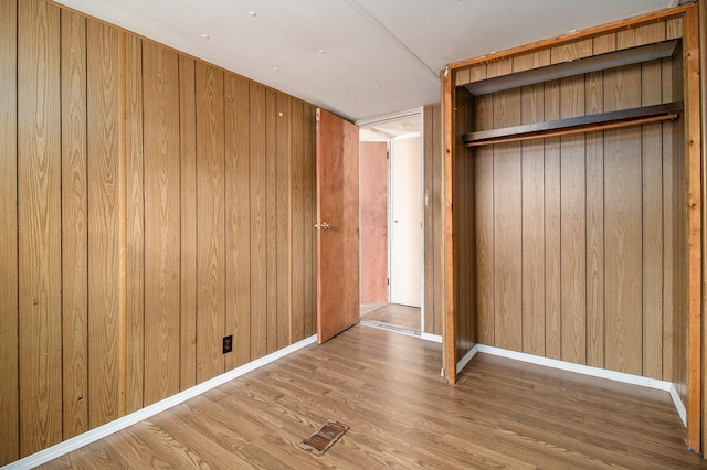 unfurnished bedroom with wood walls, wood-type flooring, and a closet