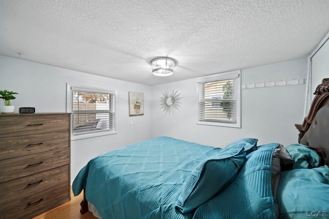 bedroom featuring multiple windows, a textured ceiling, and hardwood / wood-style flooring