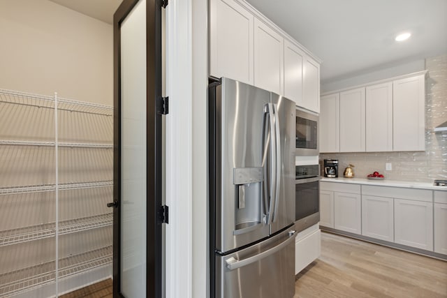 kitchen featuring light wood-type flooring, tasteful backsplash, white cabinetry, appliances with stainless steel finishes, and light countertops