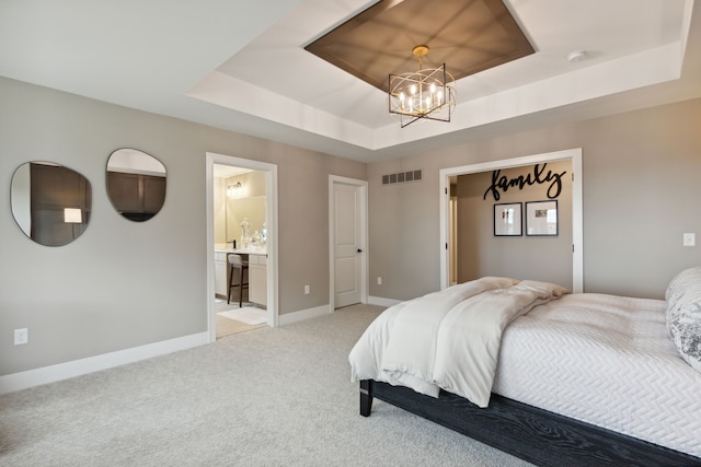 carpeted bedroom with a tray ceiling, an inviting chandelier, and ensuite bathroom