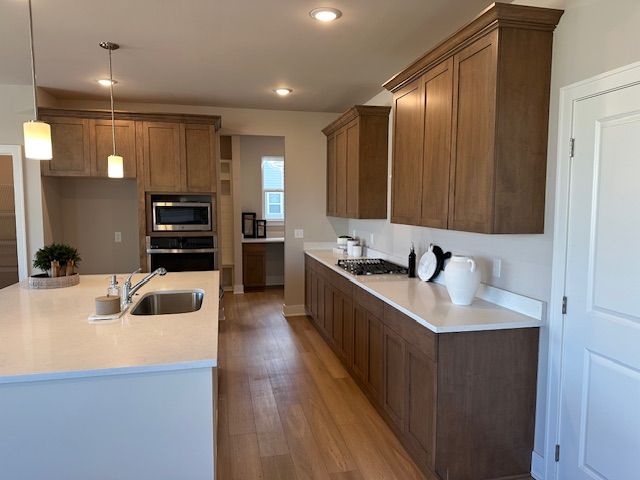 kitchen featuring light wood finished floors, a sink, hanging light fixtures, light countertops, and appliances with stainless steel finishes